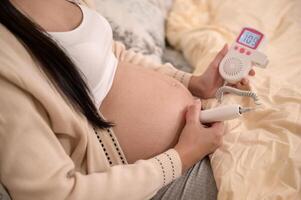 lindo grávida mulher segurando bolso fetal doppler para ouço Bêbês batimento cardiaco em barriga, fertilidade infertilidade tratamento, fertilização in vitro, futuro maternidade conceito foto