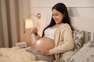 lindo grávida mulher usando lanterna em barriga para estimular uma Bêbês desenvolvimento, fertilidade infertilidade tratamento, fertilização in vitro, futuro maternidade conceito foto