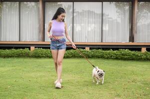 feliz ásia mulher jogando com fofa inteligente pug cachorro cachorro dentro a quintal foto