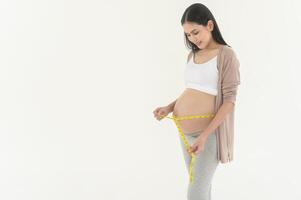 grávida mulher usando medindo fita para Verifica Tamanho do barriga gravidez e bebê desenvolvimento foto