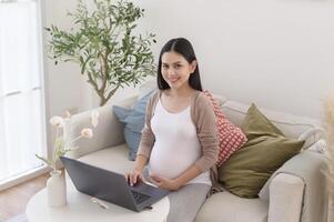 grávida mulher trabalhando em computador portátil e inteligente telefone dentro a vivo quarto às casa foto