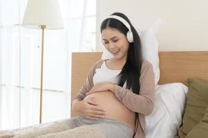feliz grávida mulher com fones de ouvido ouvindo para Mozart música e deitado em cama, gravidez conceito foto