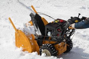 trabalhador é usando snowblower máquina para Claro neve a partir de estacionamento depois de inverno furacão em ensolarado dia foto