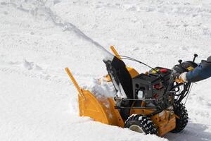 operador máquina usando snowblower para retirar neve a partir de estrada depois de inverno tempestade, Claro neve em ensolarado dia foto