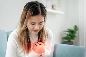 mão aguarde peito com coração ataque sintomas, ásia mulher ter peito dor causou de coração doença, vazar, dilatação, ampliado coronário coração, pressione em a peito com uma doloroso expressão foto