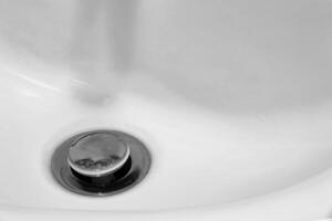 detalhe do uma cerâmico branco Pia dentro uma moderno banheiro com cromada banhado drenar. horizontal. para texto. foto