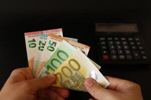 homem contando euro dinheiro com dele mão. euro notas. a papel moeda do europeu União .calculadora dentro a fundo. foto