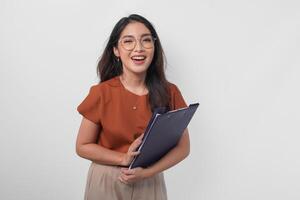 atraente sorridente ásia mulher vestindo Castanho camisa e Óculos segurando documento livro isolado sobre branco fundo. foto