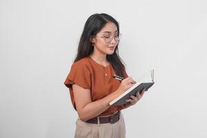 jovem ásia mulheres segurando livro e caneta escrevendo tarefa e Nota dentro a caderno em pé sobre branco fundo. foto