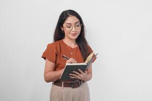 jovem ásia mulheres segurando livro e caneta escrevendo tarefa e Nota dentro a caderno em pé sobre branco fundo. foto