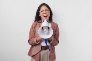 jovem ásia mulher vestindo casaco e Óculos gritando às megafone, isolado em branco fundo estúdio. foto