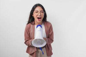 jovem ásia mulher vestindo casaco e Óculos gritando às megafone, isolado em branco fundo estúdio. foto