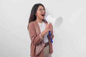 jovem ásia mulher vestindo casaco e Óculos gritando às megafone, isolado em branco fundo estúdio. foto