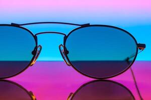 fechar-se do oculos de sol em uma espelho superfície contra uma colori gradiente fundo foto
