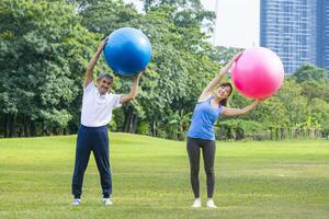 Senior ásia homem e dele filha estão exercício com ioga bola dentro público parque para Construir testemunho corpo músculo para mais velho longevidade exercício e ao ar livre exercite-se foto