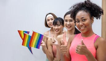 grupo de mulheres de diversidade em roupas esportivas segurando a bandeira do arco-íris lgbtq para o mês do orgulho para promover a igualdade e as diferenças do conceito homossexual e de discriminação foto