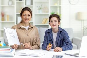 retrato do professor e estudante, fêmea mentor ensino Garoto trabalho de casa, sentado juntos às mesa dentro vivo quarto sorridente e olhando às Câmera. foto