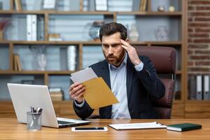 chateado e Bravo patrão recebido enviar mensagem notificação com mau notícias, masculino homem de negocios trabalhando dentro escritório com documentos e papéis, usando computador portátil às trabalhar. foto