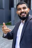 retrato do uma jovem indiano homem de negocios em pé perto a escritório construção e falando em uma ligar a partir de a telefone. fechar-se vertical foto. foto