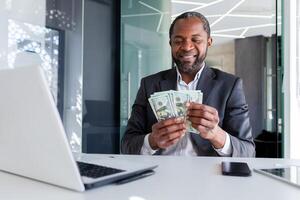 homem de negocios alegre obteve ganhar lucro renda, homem conta dinheiro nos dólares dinheiro dentro escritório às ambiente de trabalho, bem sucedido patrão feliz com realização resultados, financista banqueiro dentro o negócio terno. foto