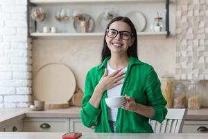 blogueiro. uma jovem lindo mulher dentro óculos e uma verde camisa senta dentro frente do uma rede Câmera às casa e registros uma blog. ele fala, gestos com dele mãos, sorri. foto