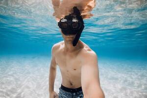 homem mergulhador dentro mascarar faço selfie embaixo da agua sobre arenoso inferior dentro azul oceano água. atividade período de férias dentro tropical mar. foto