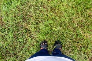 a ponto do Visão do uma homem ou mulher olhando baixa às a sandálias em pé em a Relva para fundo e cópia de espaço foto