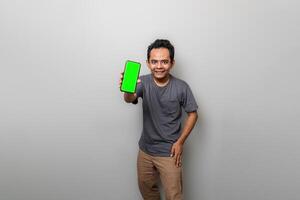 ásia homem dentro cinzento é mostrando uma verde tela Smartphone Como E se recomendando alguma coisa foto