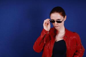 jovem mulher posando dentro vintage moda vermelho couro Jaqueta e oculos de sol foto