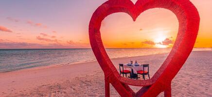 jantar de casais de lua de mel no jantar romântico de luxo privado na praia tropical nas maldivas. vista para o mar à beira-mar, costa da ilha incrível com cadeiras de mesa em forma de coração vermelho. jantar de destino de amor romântico foto