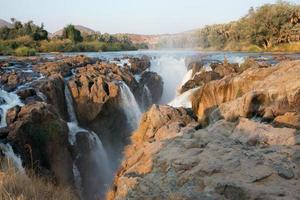 vista da epupa cai ao pôr do sol. floresta em segundo plano. namibia foto