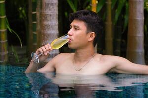 uma homem tem uma descansar dentro a piscina e desfrutando vidro do saboroso frio branco vinho durante período de férias. viagem período de férias. verão feriados. foto