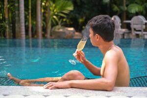 uma homem tem uma descansar dentro a piscina e desfrutando vidro do saboroso frio branco vinho durante período de férias. viagem período de férias. verão feriados. foto