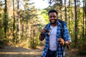 jovem homem goza usando binóculos e caminhada dentro natureza. foto