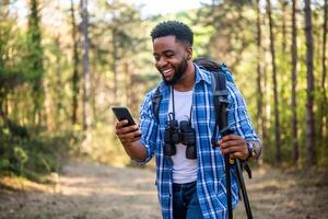 jovem homem goza caminhada e usando Móvel telefone dentro natureza. foto