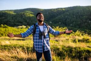 feliz jovem homem caminhante com braços elevado goza dentro a natureza. foto