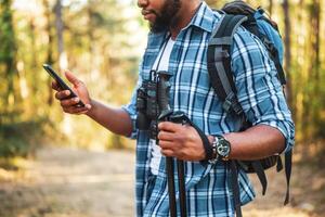 jovem homem goza caminhada e usando Móvel telefone dentro natureza foto
