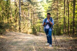 preocupado caminhante obteve perdido e ele é usando uma telefone para encontrar certo direção enquanto caminhada dentro a natureza foto