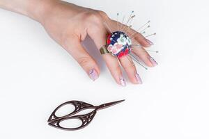 uma anel com uma pequeno travesseiro para agulhas em uma mão e tesouras em uma branco fundo foto