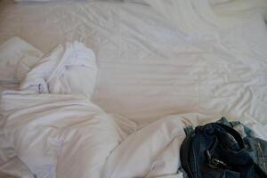 uma branco cama com amarrotado folhas e almofadas é a focal ponto do isto quarto. foto