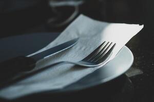 metal faca e garfo em uma lenço de papel papel e prato em uma de madeira mesa. foto