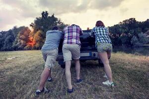 grupo do amigos empurrando a quebrado carro foto