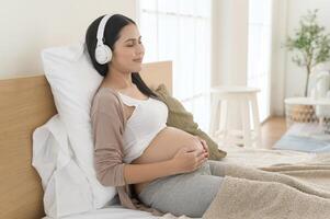 feliz grávida mulher com fones de ouvido ouvindo para Mozart música e deitado em cama, gravidez conceito foto