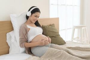 feliz grávida mulher com fones de ouvido ouvindo para Mozart música e deitado em cama, gravidez conceito foto