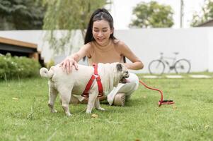 feliz ásia mulher jogando com fofa inteligente pug cachorro cachorro dentro a quintal foto