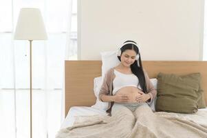 feliz grávida mulher com fones de ouvido ouvindo para Mozart música e deitado em cama, gravidez conceito foto