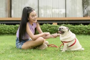 feliz ásia mulher jogando com fofa inteligente pug cachorro cachorro dentro a quintal foto