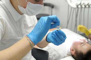 enfermeira espalhando cola em falso dentes para estar colado para uma paciente uma médico dentro amarelo luvas a assistente dentro azul frente dentes próteses temporário mandíbula falso dentes foto