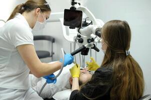 dental o mais novo escritório Novo equipamento próteses canais recheios moderno dental equipamento médio tiro do fêmea dentista dentro Preto casaco, mascarar e luvas usando dental microscópio para examinar pacientes dentes foto