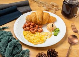 chifre croissant conjunto com omelete, feijões, cereja tomate, colher e garfo servido dentro prato isolado em de madeira mesa lado Visão do Taiwan Comida foto